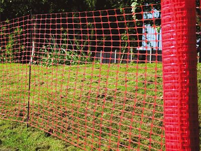 A roll of rectangular warning barrier fence is unfolding in front of the grassland.