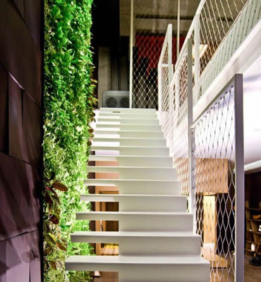 Stainless steel ferrule rope mesh is installed as balustrade infill of white stairs with green plants beside it.