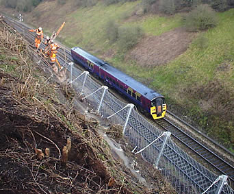 Stainless steel safety net mounted halfway down to the hill to protect the below train and train tracks from being damaged by falling rocks.